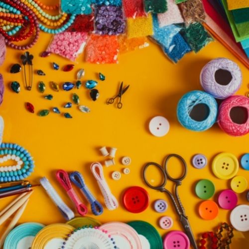 A random selection of craft supplies including scissors, string, buttons, pins, beads and ribbon. 