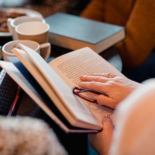 Person holding book open with one hand on top of the pages.